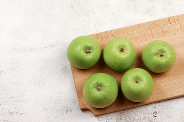 Green apples on a wooden cutting board on a light gray background. Top view, flat lay