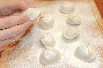 female hands sculpt homemade dumplings on a wooden board close-up