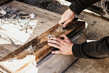 male hands screw a bolt with a screwdriver into a wooden board.