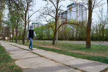 child girl walks down the street during the day, a pedestrian walkway and high-rise buildings with apartments, a residential area, a medical mask on her face protects against viruses and dust