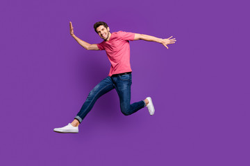 Fototapeta na wymiar Full body profile photo of attractive guy jumping high up running shopping center sale season see friend street wear casual pink t-shirt jeans shoes isolated purple color background