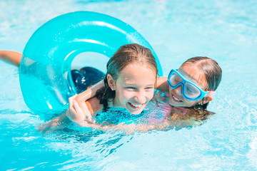 Adorable little sisters play in outdoor swimming pool