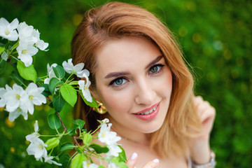 Beautiful teen redhead girl enjoying life in spring blossoming garden against blooming trees. Young dreamy thoughtful lady in nature at sunset. Springtime at countryside concept