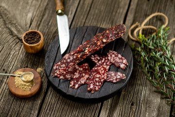 Fototapeta na wymiar Dried sausage on wooden board rosemary pepper spices wooden texture cuisine