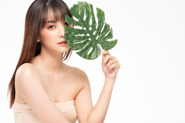 Beauty asian woman  brown hair looking smile in camera happiness and holds a large green tropical leaf in hands and covers a part of her face and cheerful with make up brush,Beauty Concept.