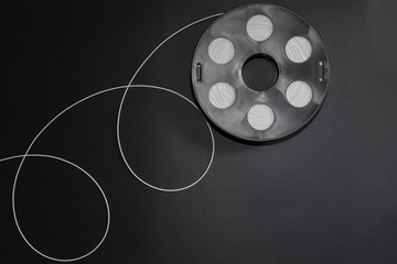 Black coil with white plastic, 3D printing filament reel for 3d printers  and with a geometric pattern of loops are on a black background.
