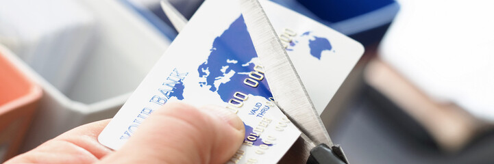 Male hand cutting banking card with scissors