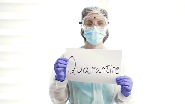 Portrait of a doctor in a protective suit with a poster QUARANTINE.