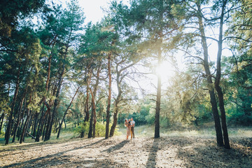 Fototapeta na wymiar Young happy family walking outdoors in the forest. Parents holding the baby in their arms and having fun. They are happy together. Smiling at each other and looking forward