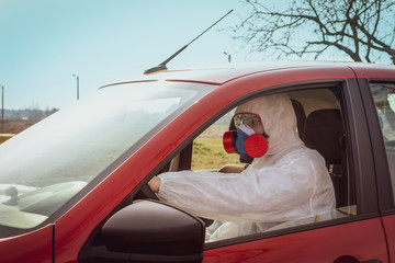 man sits in a car in a protective suit, goggles and a mask for respiratory protection