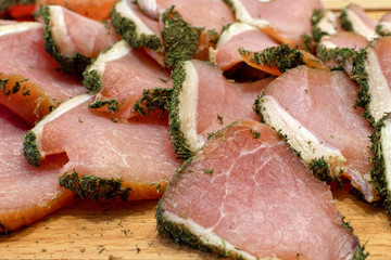 Sliced ​​jerky. Sliced ​​dried meat in green spices on wooden board close-up