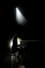 Female keyboards player on stage during concert, backlight