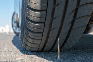 puncture wheel concept. the self-tapping screw lies on asphalt under a car wheel