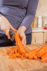 Kobiece dłonie obierają marchew za pomocą obieraczki do warzyw. - obrazy, fototapety, plakaty