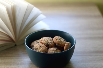 Bowl of chocolate chip cookies and open book on a table. Selective focus.