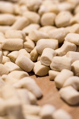 Fresh homemade uncooked gnocchi Italian dumplings on a floured wooden board in a kitchen with fresh basil behind in a close up view.