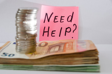 The inscription "need help" on the sticker on the background of euro banknotes and a stack of coins.