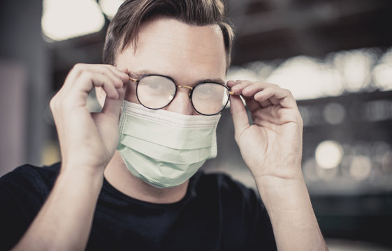 young attractive man with blue eyes and glasses puts on a respirator mask with fogged glasses