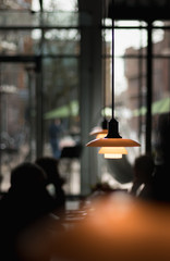 Ambience image of a lunchroom with the focus on the pendant lights, people are visible in the...