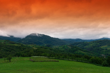 Fototapeta na wymiar Mountain landscape with red sky and green field.