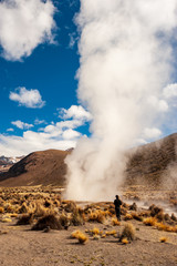 Man walking towards huge geyser. Trekker at Hot spring and geyser at Sajama National Park in Bolivia. Geothermal activity andean geysers in geysers valley, Sajama, Bolivia, South America