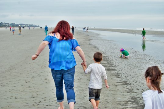 Mother And Two Young Children Walking And Playing On The Beach Photo Taken From Behind No Recognizable People