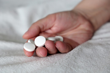 White pills in a palm of female hand on the bed. Concept of medication, vitamins or sleeping pill