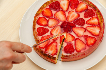 Hand slicing delicious homemade strawberry tart. Isolated on wooden background. Top view. Close-up. Horizontal shot.