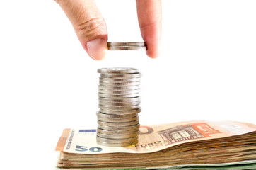 put a coin on a stack with coins on euro banknotes. White background. Money saving concept....