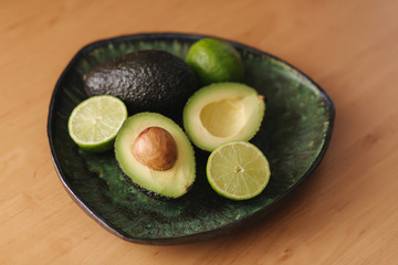 Avocado and lime halves on green plate. Vegetarian food concept