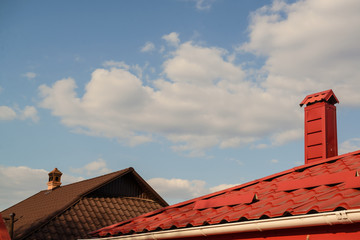 Red roof of a house on a blue sky with clouds