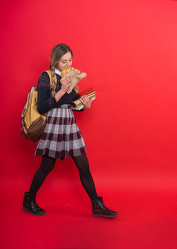 Schoolgirl in uniform with a backpack comes and eats at the same time, she keeps books, long braids