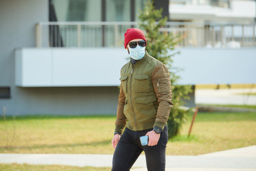 A man in a medical face mask to avoid the spread coronavirus holding his smartphone in a cozy...