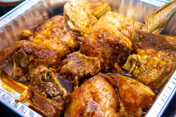 Close up view of marinated raw chicken pieces with various spice and sauce in a aluminum food container before grill in oven.