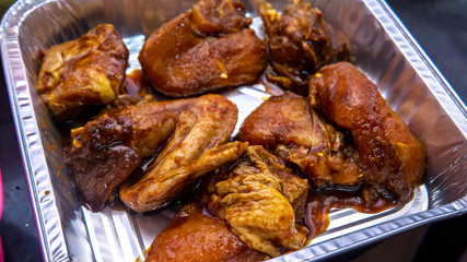 Close up view of marinated raw chicken pieces with various spice and sauce in a aluminum food container before grill in oven.