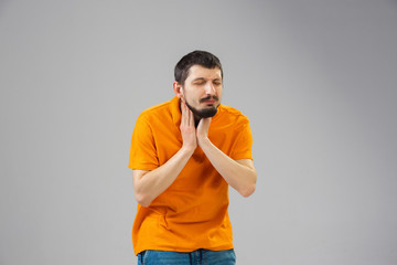 Young caucasian man suffers from a sore throat, feels sick, ill and weakness isolted on gray studio background. Symptoms of desease or unhealthy lifestyle. Sickness, ilness, sad and upset. Copyspace.