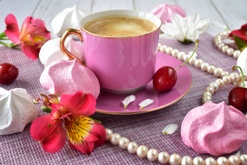 Obraz na płótnie Canvas Pink ceramic cup with coffee on a small saucer, marshmallows and flowers on the table