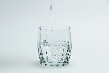 Water is poured into a transparent glass on a white background