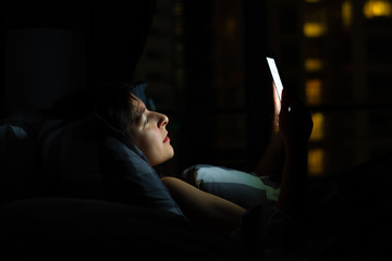 Girl on the bed before falling asleep looks at a smartphone. Check news and social networks before going to bed. Smart gadget