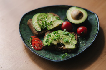 Vegetarian breakfast at home. Sandwich with fresh sliced avocado above rye bread with cherry tomatoes on green plate