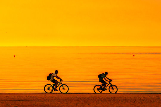 Biker silhouette riding along beach at sunset on bike Sporty company group of friends on bicycle outdoors Success achievement accomplishment and winning concept with cyclist mountain biking Copyspace