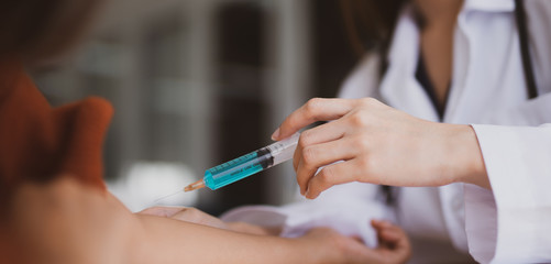 Doctor making an injection with a syringe patient receiving vaccine shot in hand while sitting on hospital