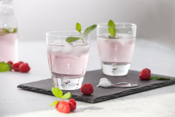 Glasses of raspberry infused water  with raspberries, ice and fresh mint leaves  on concrete background stone strong light with glass shadows. Copy space. 