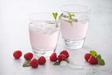 Glasses of raspberry infused water  with raspberries, ice and fresh mint leaves  on concrete background stone strong light with glass shadows. Copy space. 