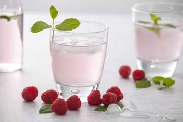 Glasses of raspberry infused water  with raspberries, ice and fresh mint leaves  on concrete background stone strong light with glass shadows. Copy space. 