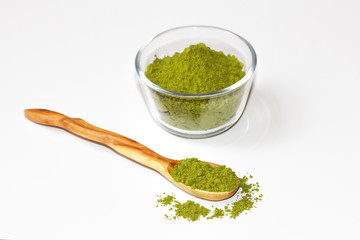 Green tea matcha in a glass bowl and a wooden spoon on a white background close-up. Useful tea matcha macro.