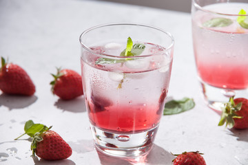 Glasses of strawberry water  with strawberries, ice and fresh mint leaves  on concrete background stone strong light with glass shadows. Copy space. Close up