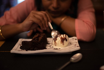 Blurred half face portrait of an Indian woman eating ice cream and brownie with a spoon inside a cafe or ice cream parlor. Indian lifestyle