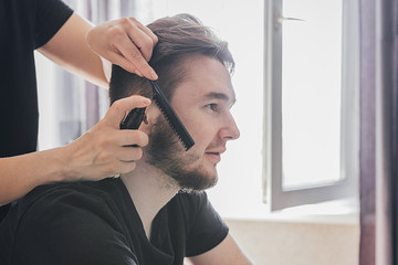 Fototapeta premium man with a beard cuts and cares for the hair himself in a quarantine coronavirus pandemic covid 19, the concept of stay home, a home hairdresser