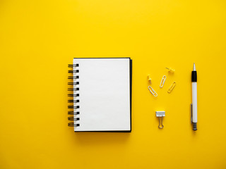 Ein leerer Notizblock, ein Kugelschreiber und Büroklammern auf einem gelben Schreibtisch, Flat lay